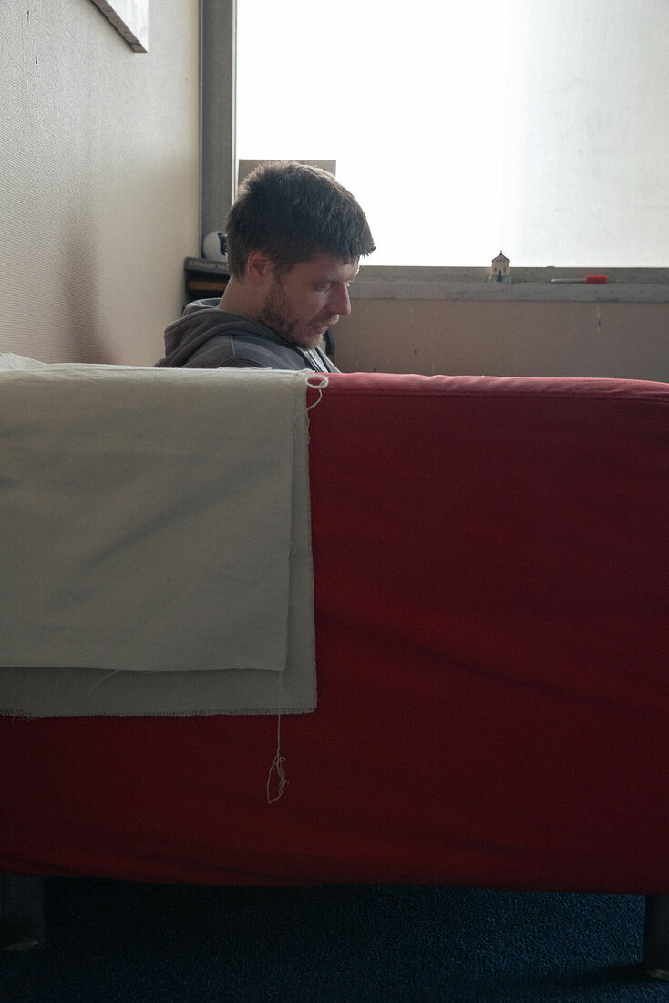 Vasily sitting in the sofa in his room he has in squat in one of the office buildings in Noisy-le-Grand. March 2025.